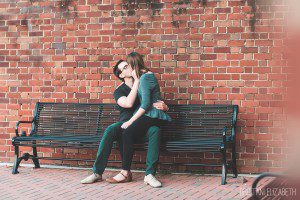 engaged couple kissing on bench against brick wall