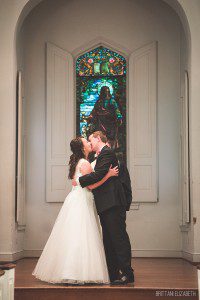 bride and groom kissing at altar stained glass window