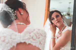 candid bride getting ready putting on earrings looking in mirror