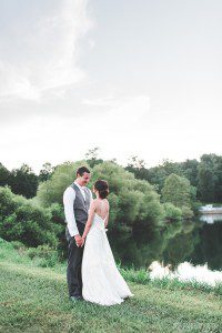 bride and groom holding hands by pond summer wedding