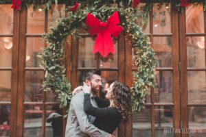 engaged couple in front of holiday wreath