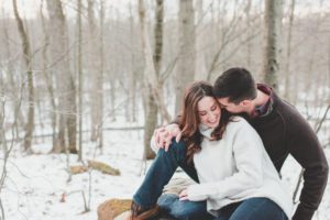 engaged couple nuzzling in snowy woods